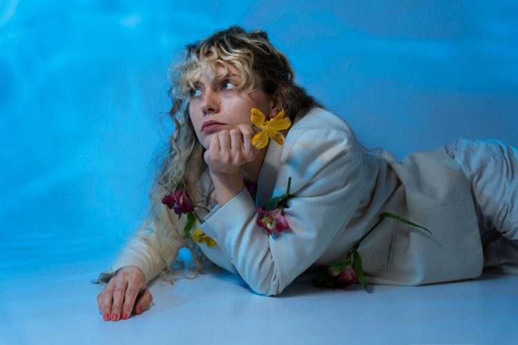 Kobieta w jasnym garniturze leżąca na niebieskim tle, ozdobiona kolorowymi kwiatami