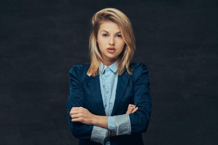 Pewna siebie młoda kobieta w eleganckiej marynarce na ciemnym tle, z założonymi rękami