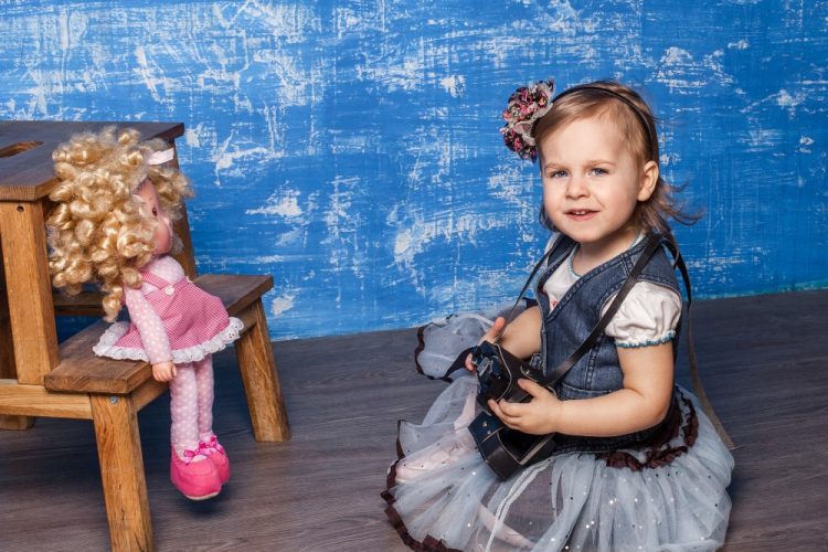 Dziewczynka podczas sesji dziecięcej z aparatem w ręku, fotografująca lalkę – kreatywna fotografia w studiu, Fotografia Olivia