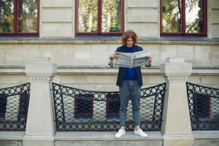 Młody mężczyzna z długimi włosami czytający gazetę na tle zabytkowego budynku