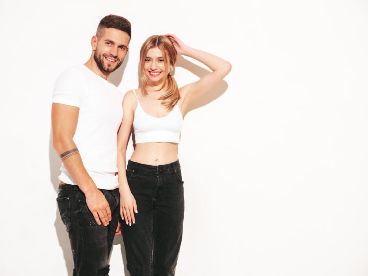 Uśmiechnięta para ubrana w białe i czarne stylizacje na tle białej ściany