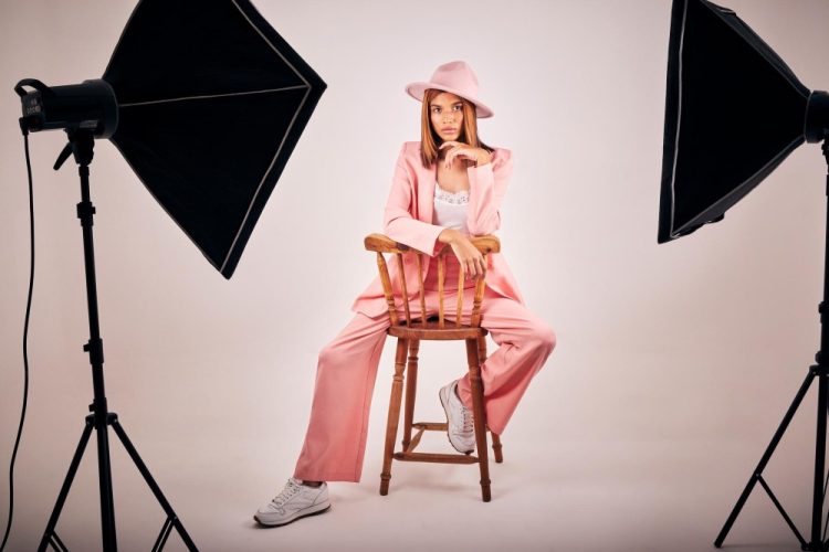 Młoda kobieta w różowym garniturze i kapeluszu pozuje na krześle w profesjonalnym studio fotograficznym