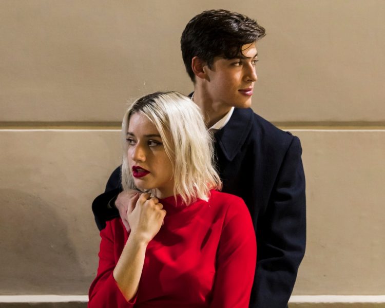 Para młodych ludzi w eleganckich ubraniach, stojąca przy ścianie, kobieta w czerwonej sukience, mężczyzna w ciemnym płaszczu