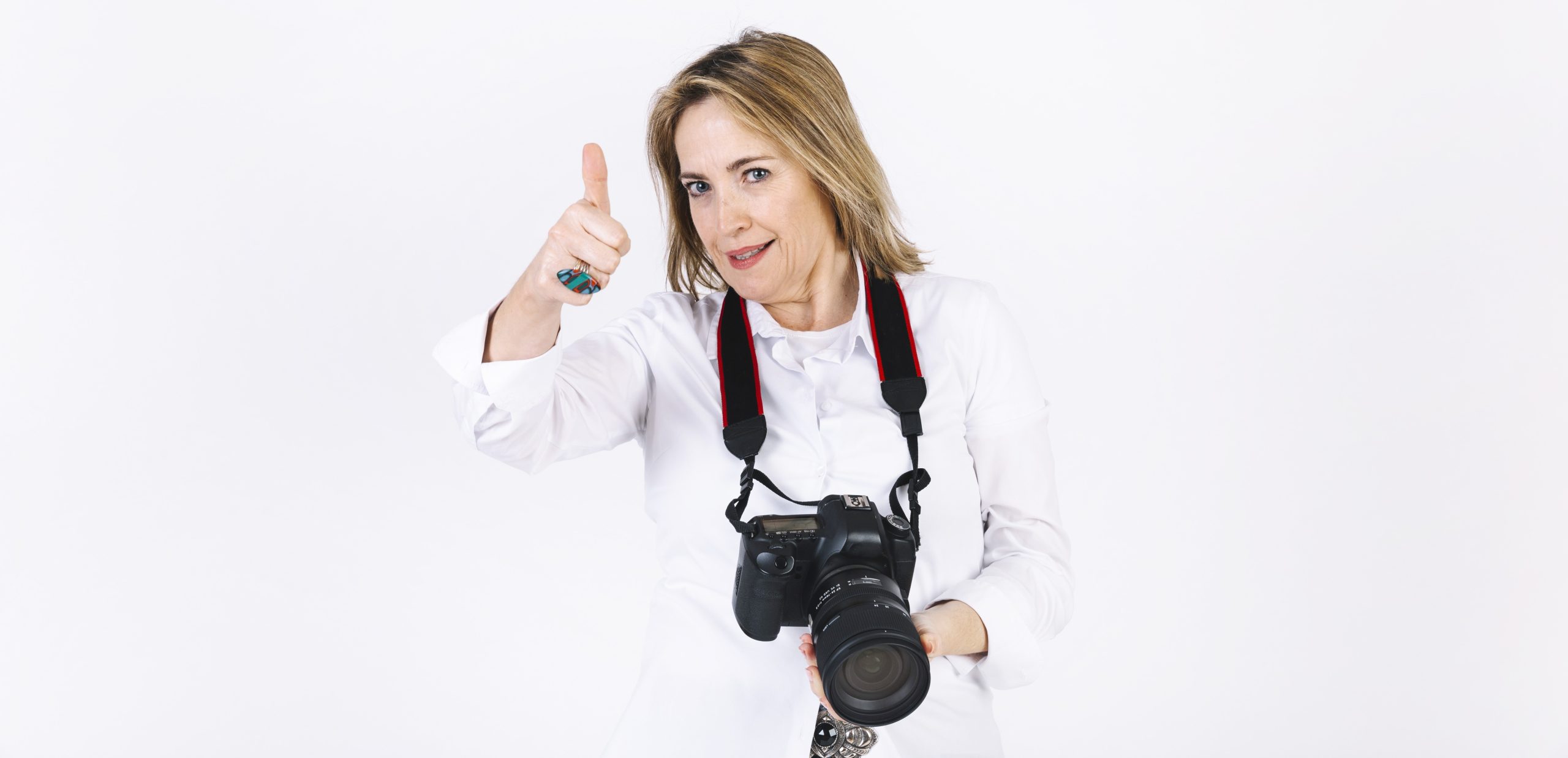 Uśmiechnięta kobieta fotograf w białej koszuli pokazuje kciuk w górę i trzyma profesjonalny aparat