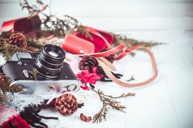 Klasyczny aparat analogowy otoczony szalikiem, szyszkami i zimowymi dekoracjami na białym tle.